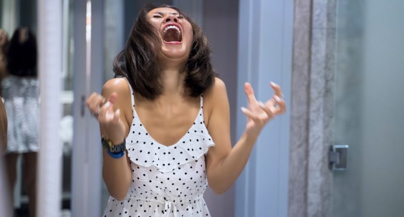Woman in polka dot dress shouting at her reflection in a mirror.