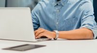 Portrait of cheerful young businessman working on his laptop in a co-working space. Modern businessman smiling while typing on his laptop. Happy entrepreneur sitting in an office.