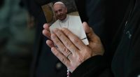 A woman's hands are clasped in prayer around a photo of Pope Francis