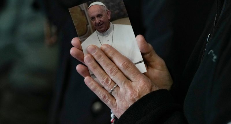 A woman's hands are clasped in prayer around a photo of Pope Francis