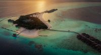 An airplane is approaching a tropical paradise island in the Maldives with turquoise during a colorful sunset
