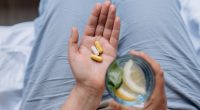 Woman's hand holding capsules and a glass of water with lemon.