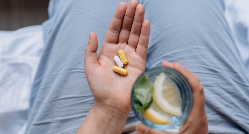 Woman's hand holding capsules and a glass of water with lemon.