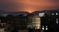 Nighttime view of Sana'a, Yemen, with an orange glow in the sky.