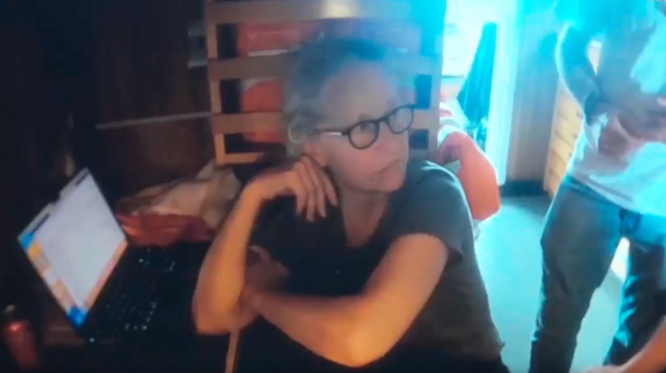 Screenshot of a woman sitting at a laptop.