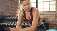 Sweaty young woman eating energy bar at gym after strong workout session. Beautiful exhausted woman enjoying chocolate bar after a heavy workout in fitness gym. Eating protein bar.