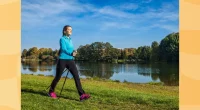 happy young woman doing Nordic walking with walking poles through park by a lake on a sunny day