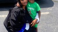 A graduating woman in a cap and gown embraces her young child.