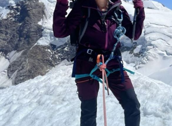 A woman mountain climber poses on a snowy peak, giving a peace sign.