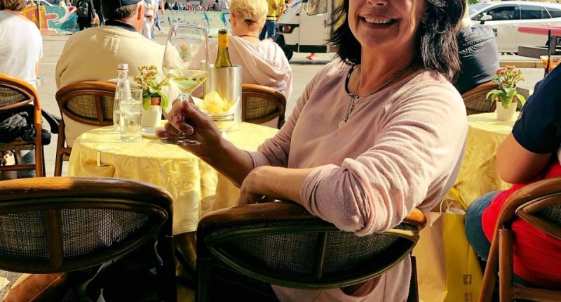 Woman sitting at an outdoor cafe with a glass of white wine, Duomo di Milano in the background.