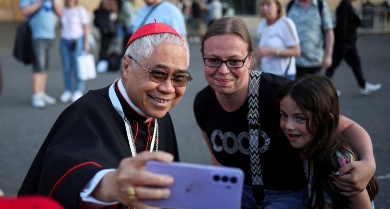 Cardinal William Seng Chye Goh taking a selfie with two women and a child in St. Peter's Square.