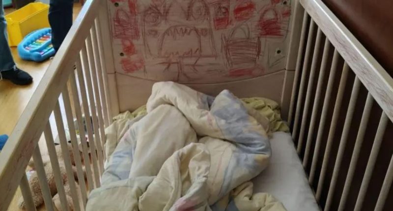 A crib with children's drawings on the headboard and bedding inside.
