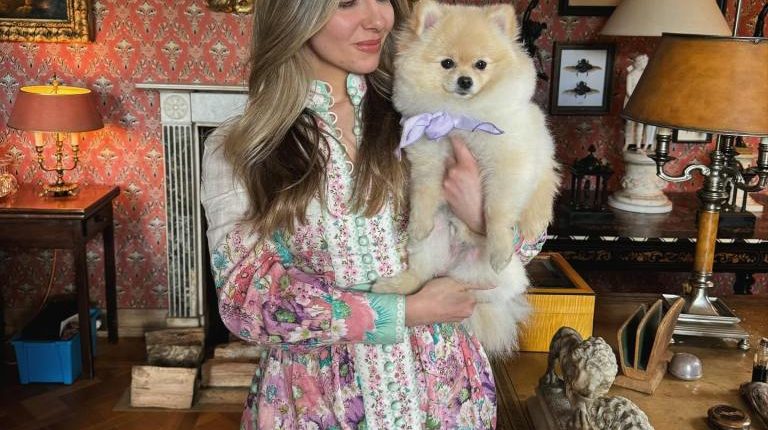 Woman in floral dress holding a Pomeranian dog.