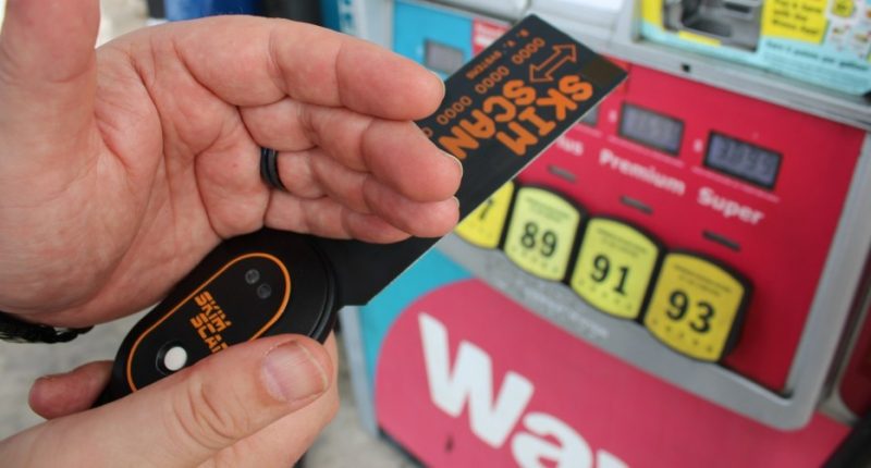 Person holding a skim reader device and gas station credit card reader at a gas pump.