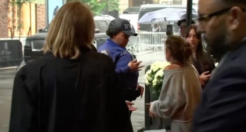 A New York City police officer speaks with a group of people near some flowers.