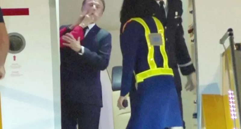 Man in suit exiting airplane, attended by uniformed personnel.