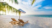 Two lounge chairs on a tropical beach under a beach umbrella.