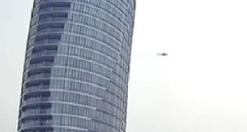 Helicopter flying near a skyscraper.