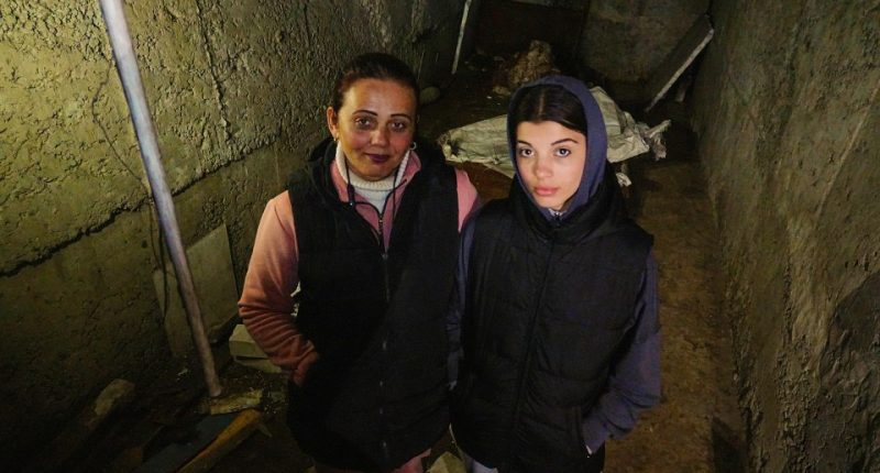Two women standing in a dark, damaged basement.