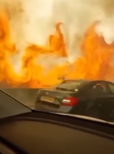 Cars driving on a highway next to a large wildfire.