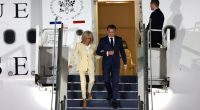 Emmanuel and Brigitte Macron disembarking from a plane.