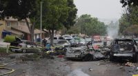 Aftermath of a small plane crash in a residential neighborhood, showing damaged cars and emergency personnel.