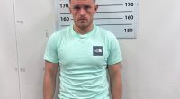 Mugshot of a man in a mint green shirt and black shorts.