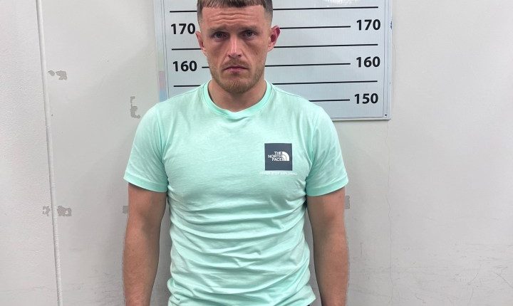 Mugshot of a man in a mint green shirt and black shorts.
