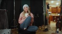 Woman holding a mug, sitting on a chair on a film set.
