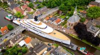 Aerial view of a mega yacht passing through a narrow canal in a Dutch village.