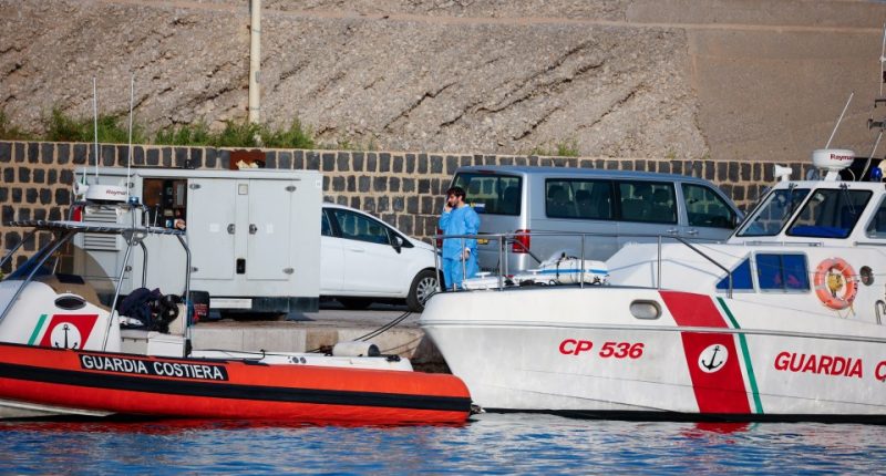 Person on phone near Guardia Costiera boat at port.