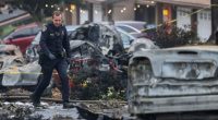 Police officer surveying the scene of a plane crash that damaged several cars.