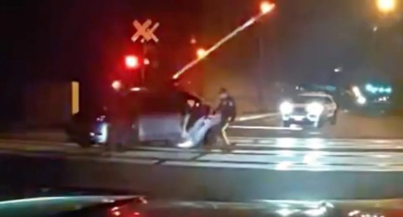 Two police officers rescuing an impaired driver from a car on train tracks.