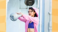 fit, determined brunette woman in pink hoodie and purple sports bra doing kettlebell swing exercises outdoors