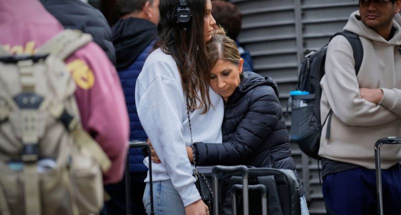 Two women embrace at a train station while waiting for news about delayed trains.
