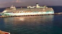 Cruise ship docked at a port with a UFO-like object zooming past.