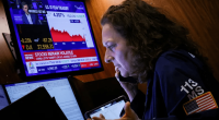 Woman on phone reviewing stock market data on monitors.