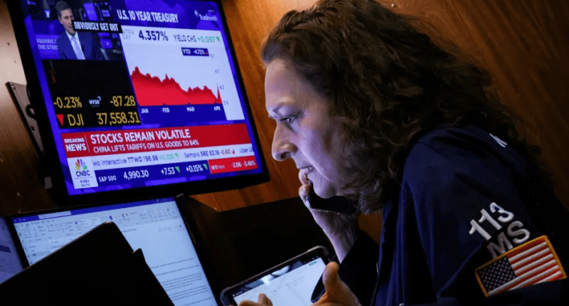 Woman on phone reviewing stock market data on monitors.
