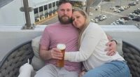 Couple cuddling on balcony overlooking city.
