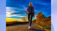 fit, middle-aged woman bundled up and walking on path by the water on fall afternoon at sunset