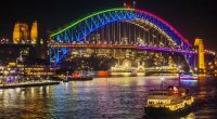 A ferry passes the Sydney Harbour Bridge, lit up in colourful lights as part of the Vivid Sydney festival.