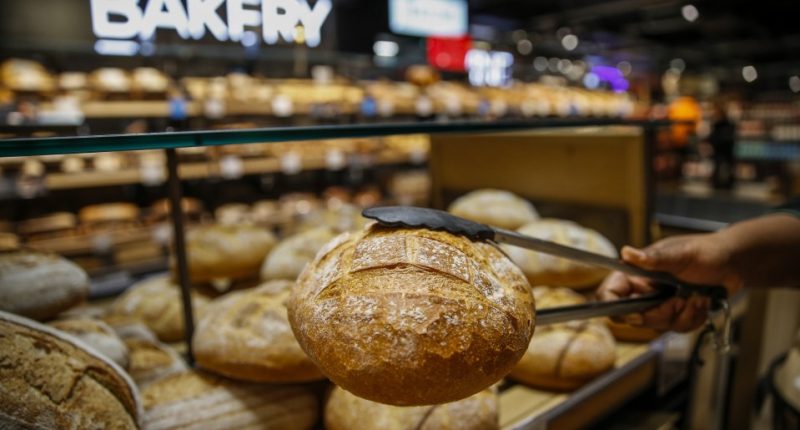 Woman reaching for bread on shelves in a bakery.