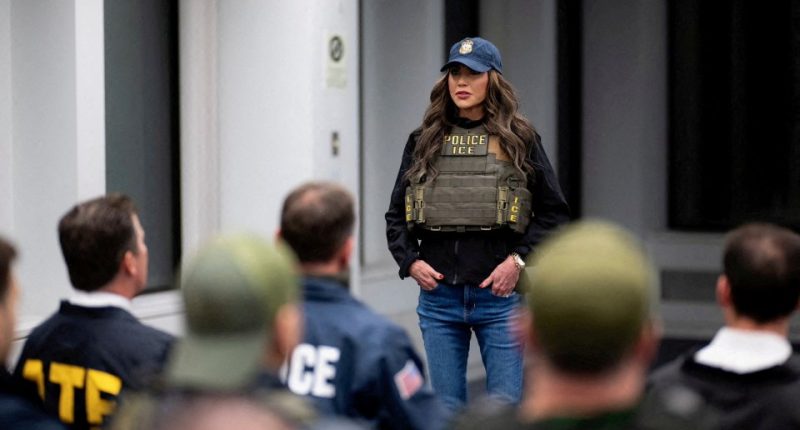 Secretary Kristi Noem in ICE vest briefing law enforcement.