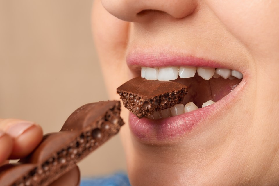 Close-up of a woman biting a piece of chocolate.