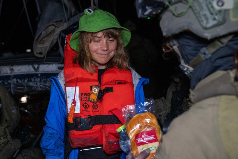 Greta Thunberg, wearing a life vest, receives food from an Israeli Defense Forces soldier after her ship was boarded.