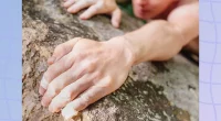 Young man climbing on rock wall, close-up of male hands with tape in magnesium powder.