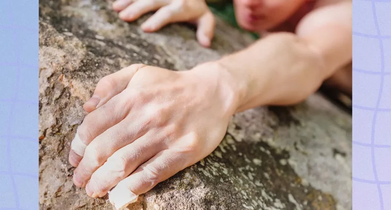 Young man climbing on rock wall, close-up of male hands with tape in magnesium powder.