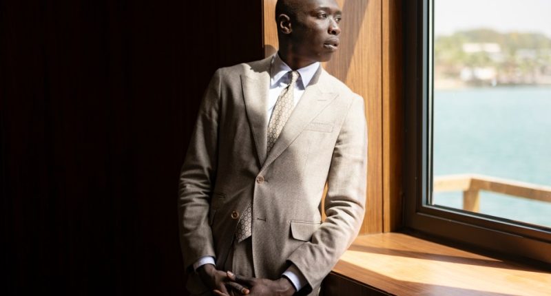 Khaby Lame in suit looking out window.