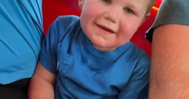 A toddler in a blue shirt sits on someone's lap.