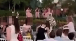 People seated at white chairs outdoors watching a performance.